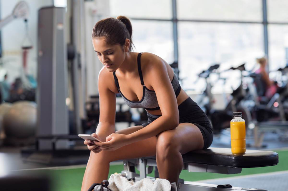 Woman sat on gym bench with bottle of orange juice next to her